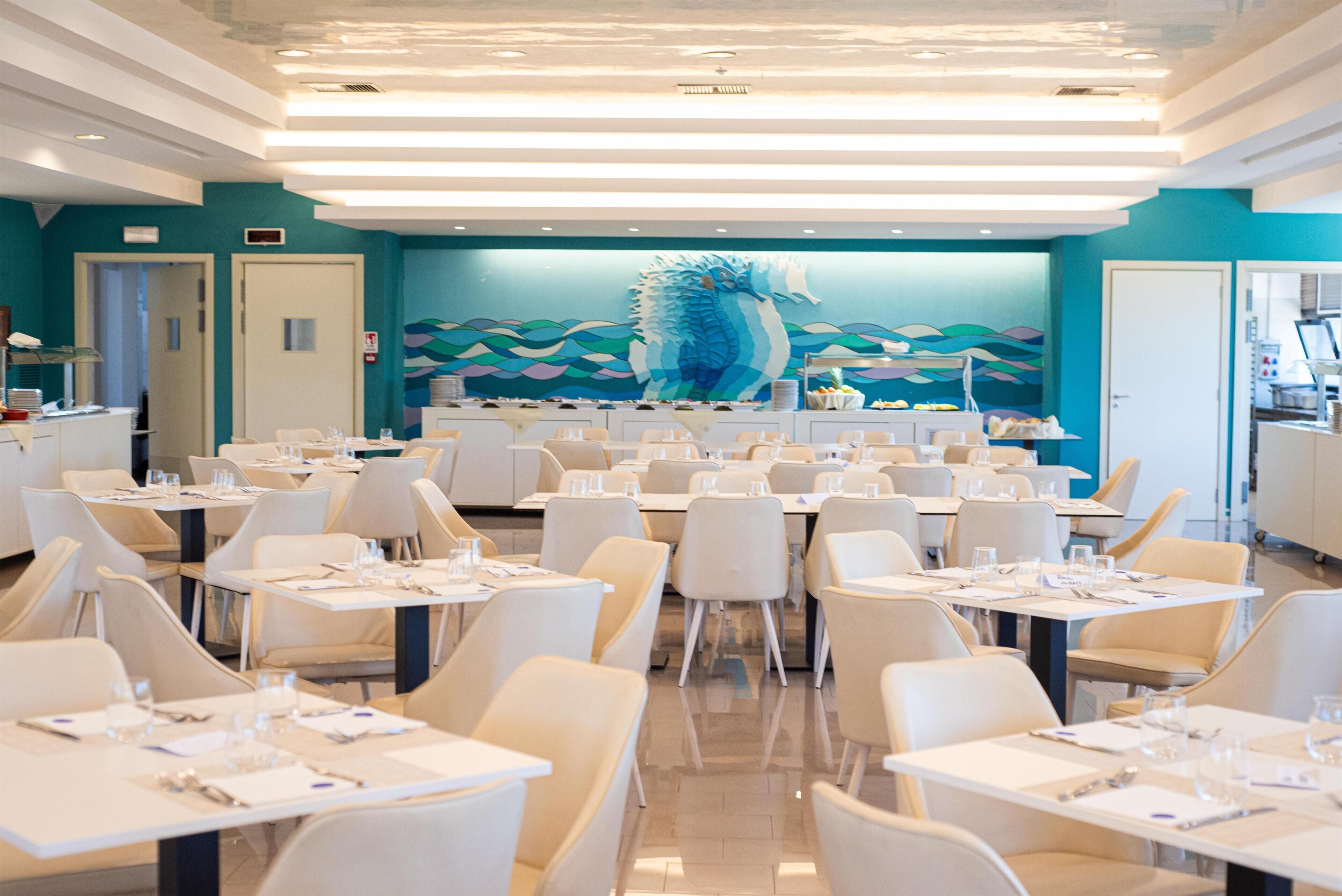 Un vaste espace dédié à la salle à manger, avec de nombreuses tables et chaises, une grande fresque murale au fond et un design moderne au niveau du plafond.