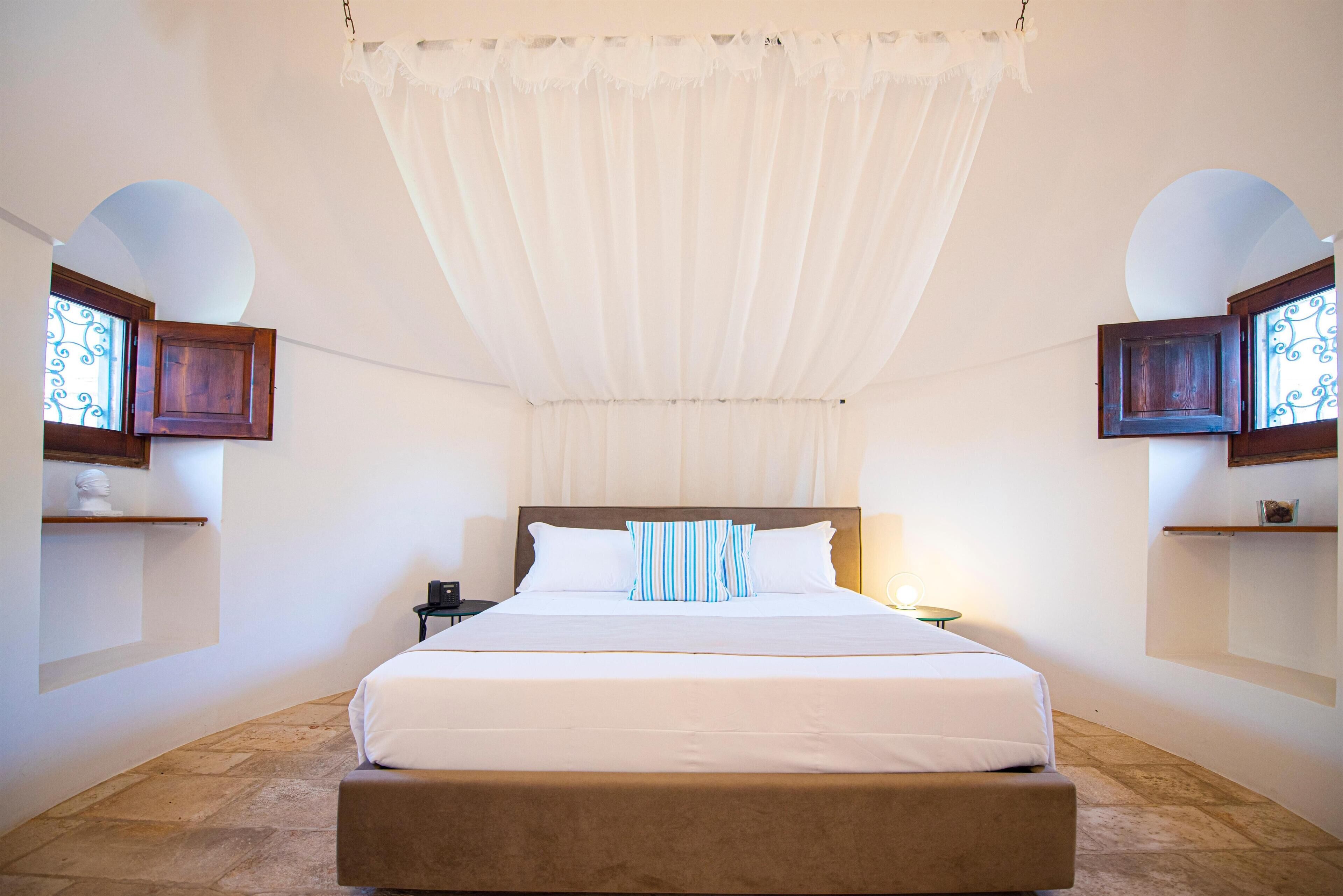 A bedroom with a large bed, a canopy, two nightstands, and decorative wall sconces.