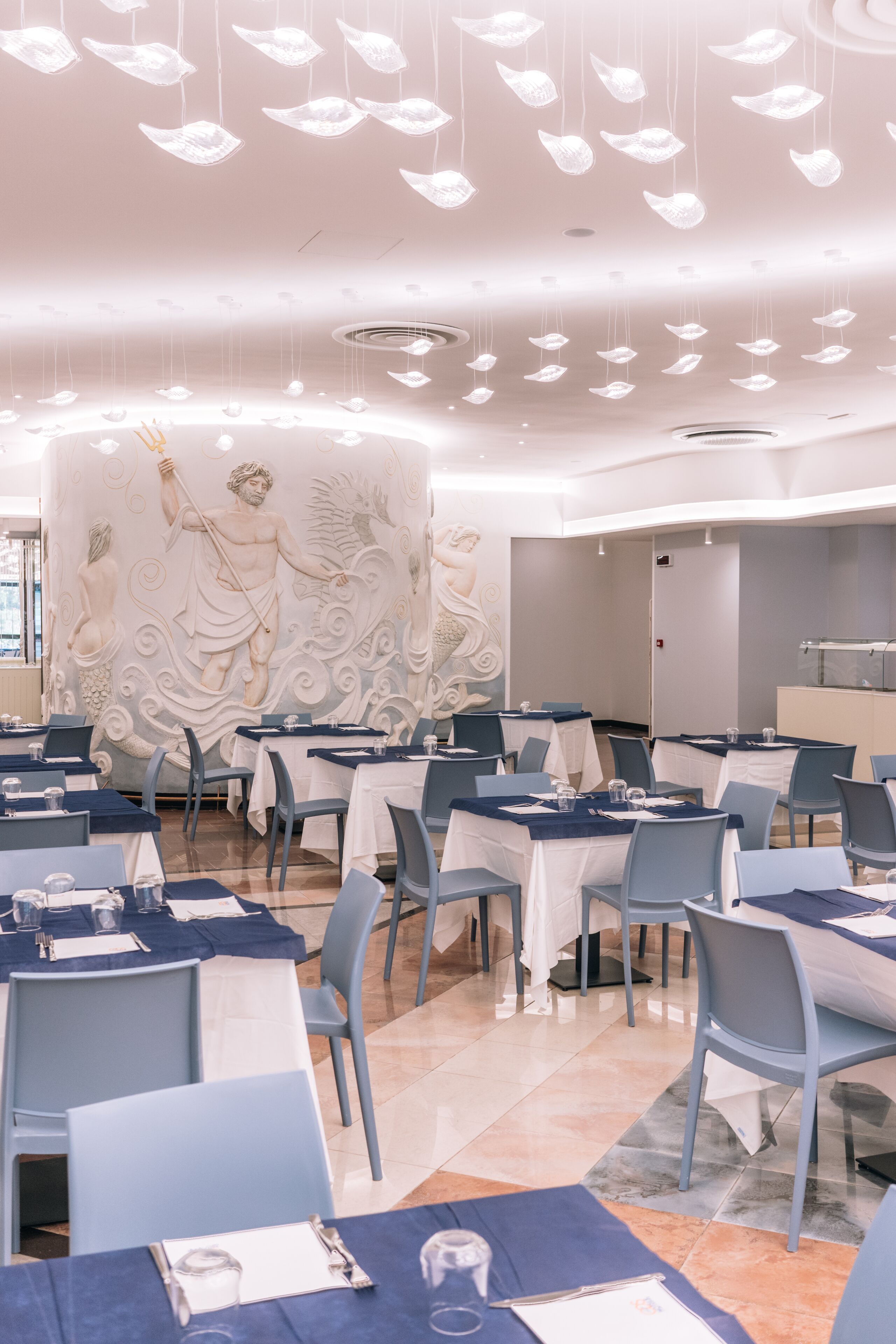 A dining area with tables set for service, a decorative wall mural, and hanging light fixtures.
