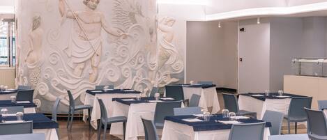 A dining area with tables set for service, a decorative wall mural, and hanging light fixtures.