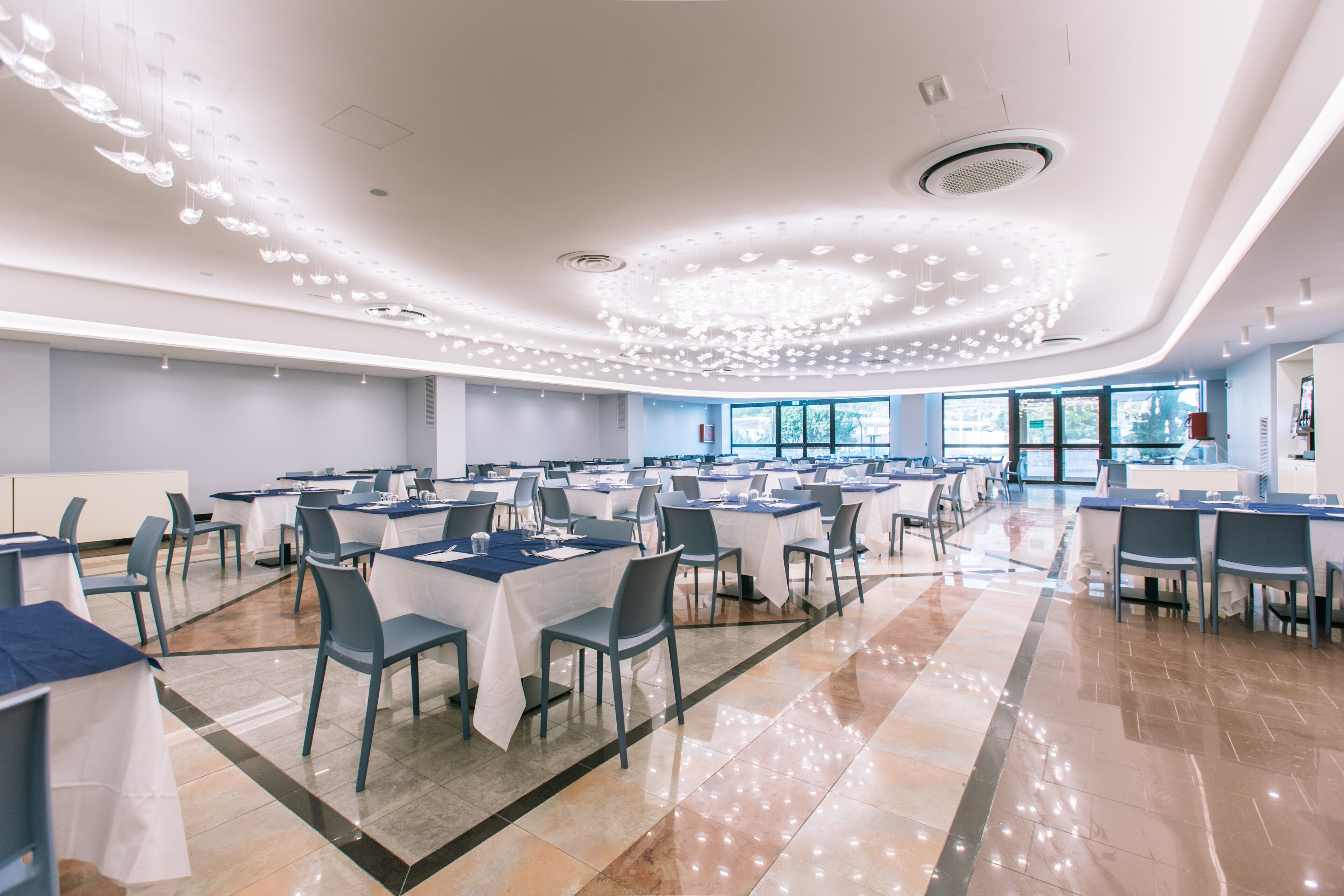 Une salle de conférence spacieuse, dotée de tables et de chaises, de grandes fenêtres et d’un design moderne au niveau du plafond.