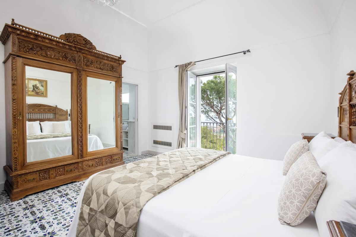 Een slaapkamer met een groot bed, een houten garderobe en een balkon met uitzicht.
