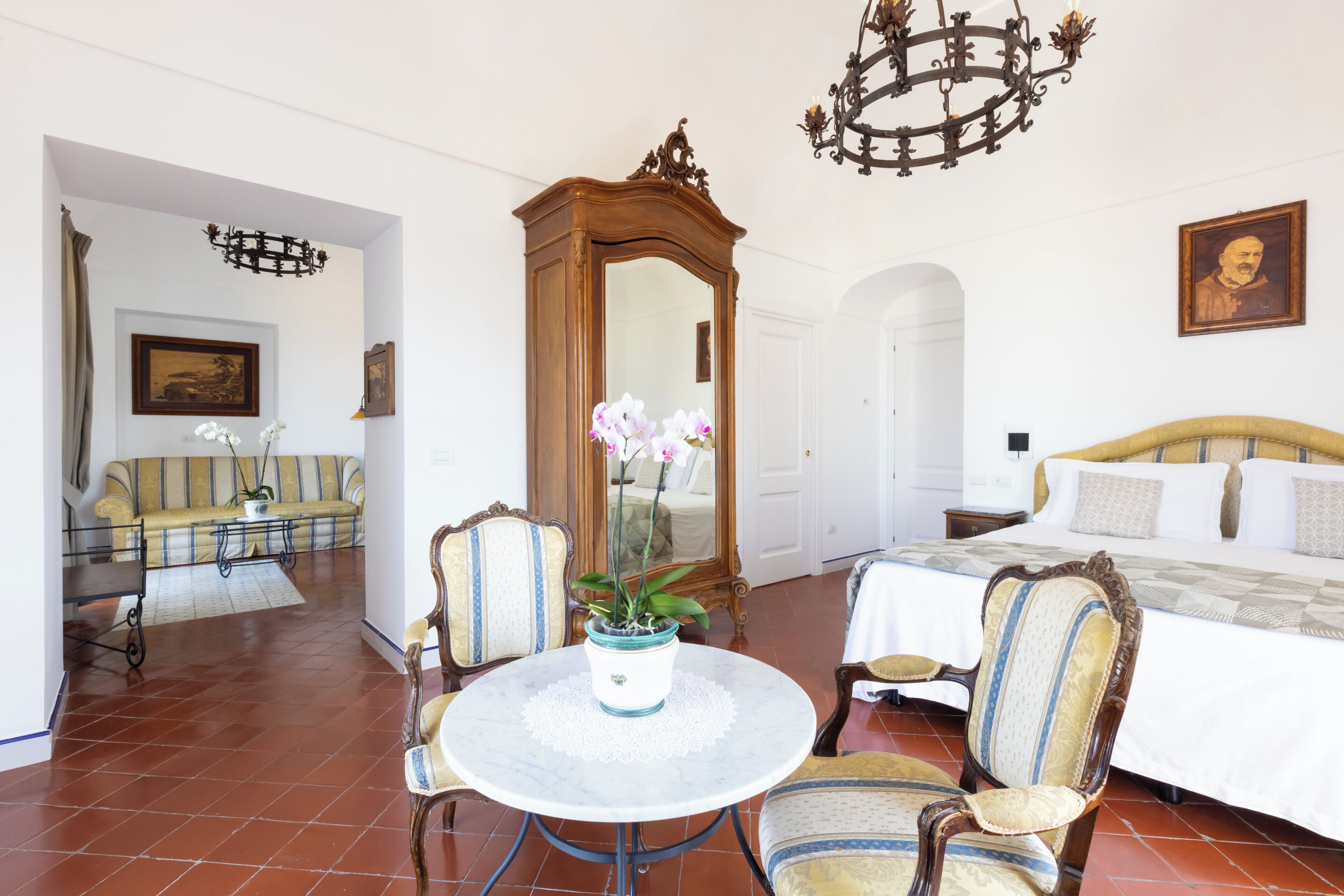 A room with a round table, two chairs, a bed, and a mirror.