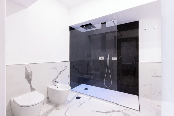 A modern bathroom with a glass-enclosed shower, a toilet, and a sink.