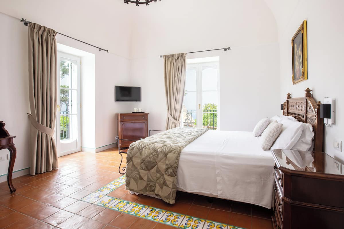 Een slaapkamer met een bed, een dressoir, een televisie en een raam met gordijnen.