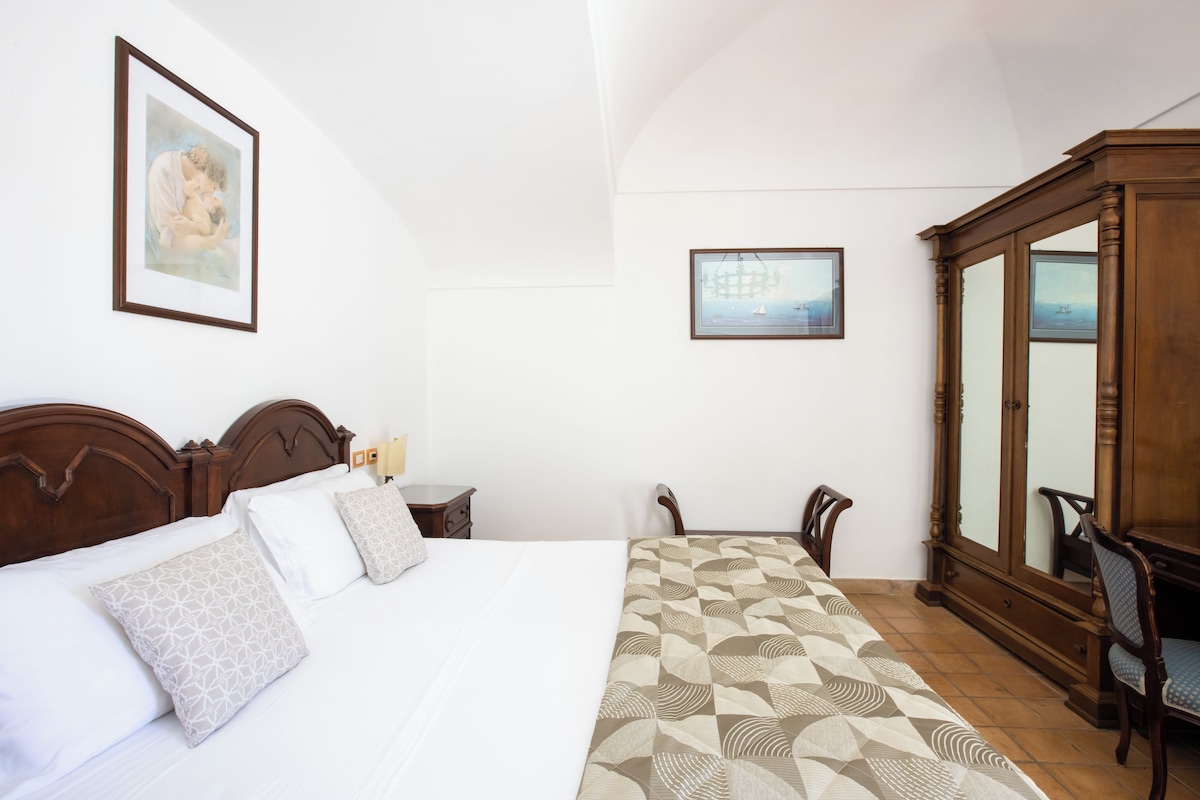 Een net opgemaakt bed met beddengoed met een patroon, een houten garderobe en twee ingelijste foto’s aan de muur.