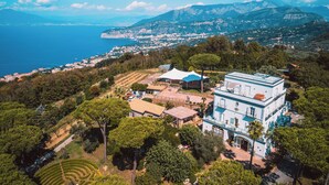 Un grand immeuble à étages, doté d’une façade bleue et blanche, entouré d’une végétation luxuriante et offrant une vue sur la côte.