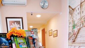 A reception area with a stone-textured counter, a clock, framed artwork, and a mural on the wall. - Hotel Everest (Rome)
