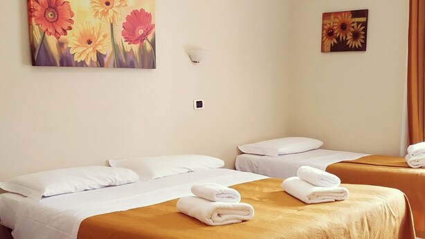 A hotel room with two beds, beige walls, and a painting of flowers. - Hotel Everest (Rome)