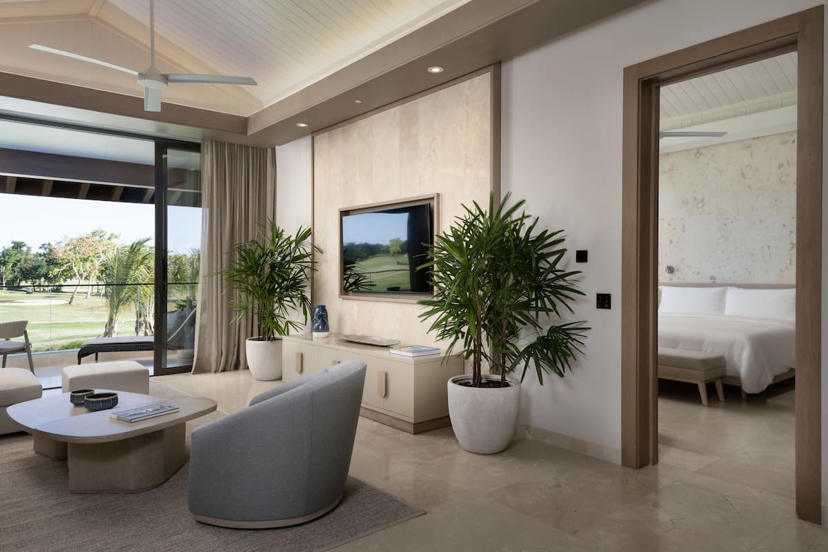 Una sala de estar moderna con un televisor de pantalla plana, asientos cómodos, una planta grande en maceta y vistas a un campo de golf.