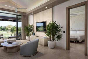 Una sala de estar moderna con un televisor de pantalla plana, asientos cómodos, una planta grande en maceta y vistas a un campo de golf.