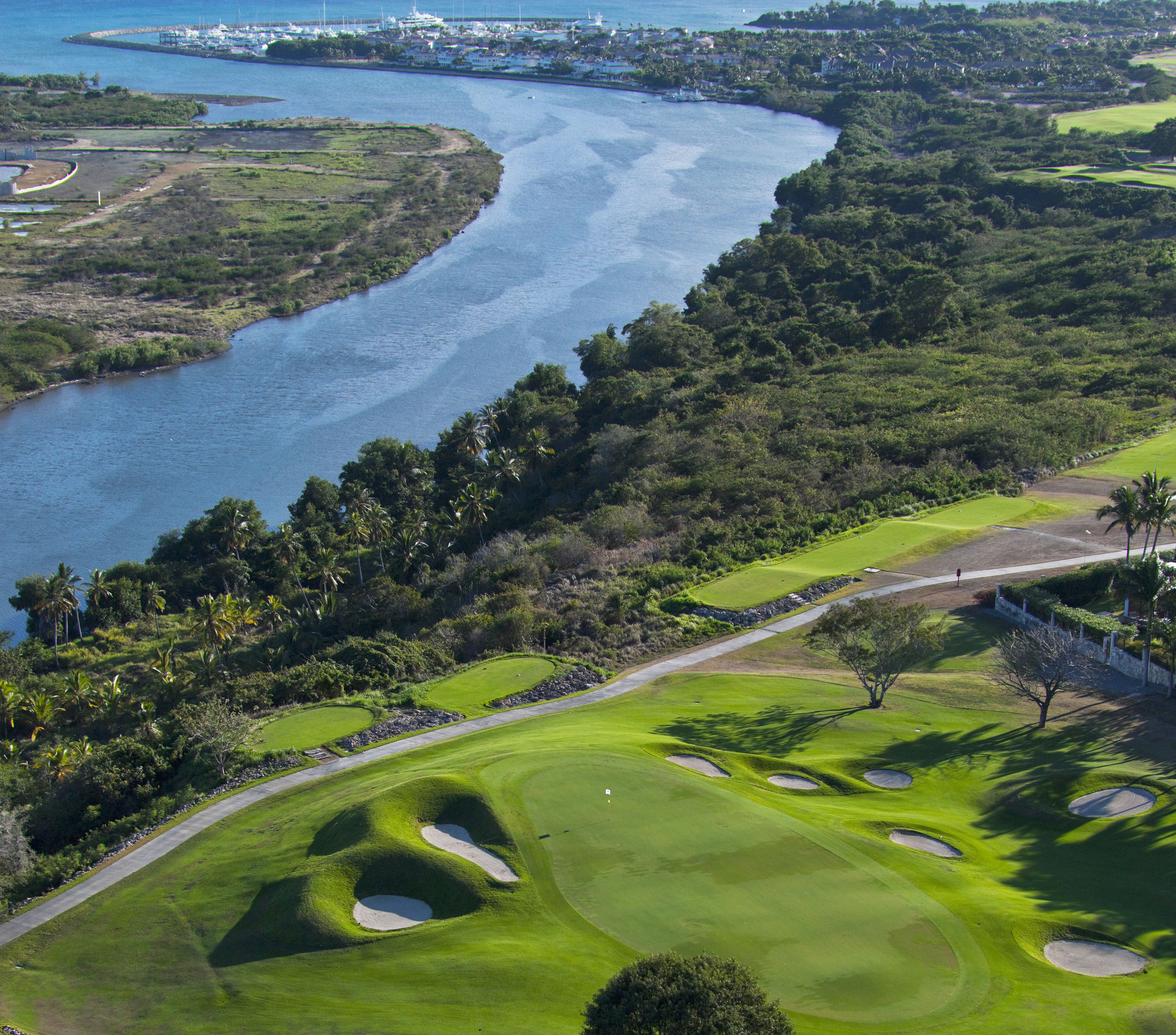 Un parcours de golf avec un plan d’eau, une végétation luxuriante et un ciel dégagé.
