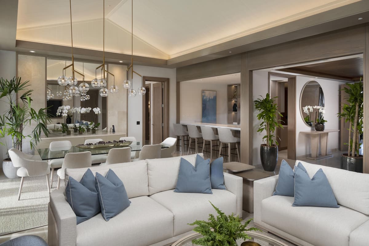Un moderno salón con un sofá blanco, cojines azules y un comedor con sillas blancas y una mesa de vidrio.