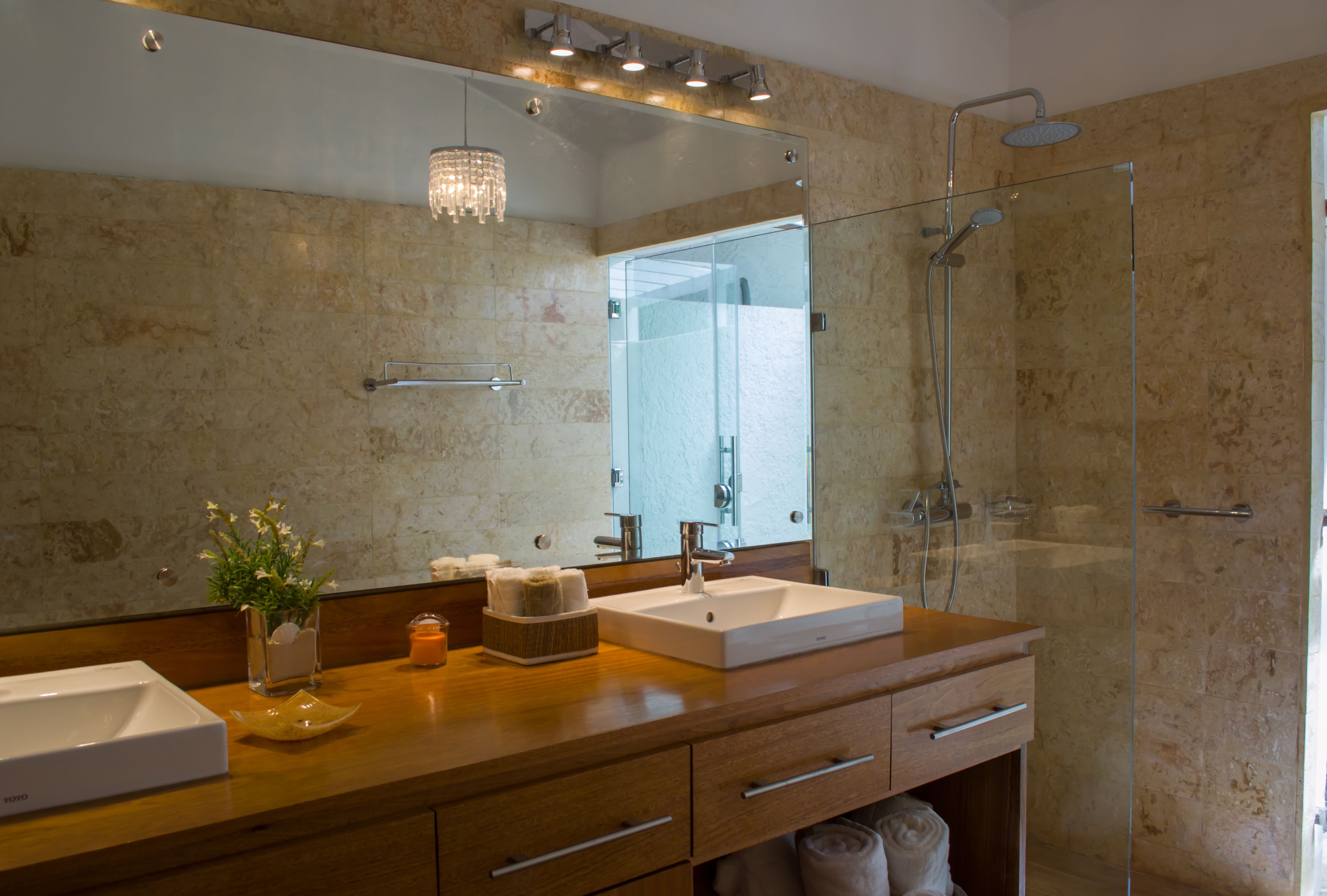 Une salle de bain moderne avec un grand miroir, une douche à parois de verre et un meuble-lavabo en bois doté d’un évier et d’un porte-serviettes.