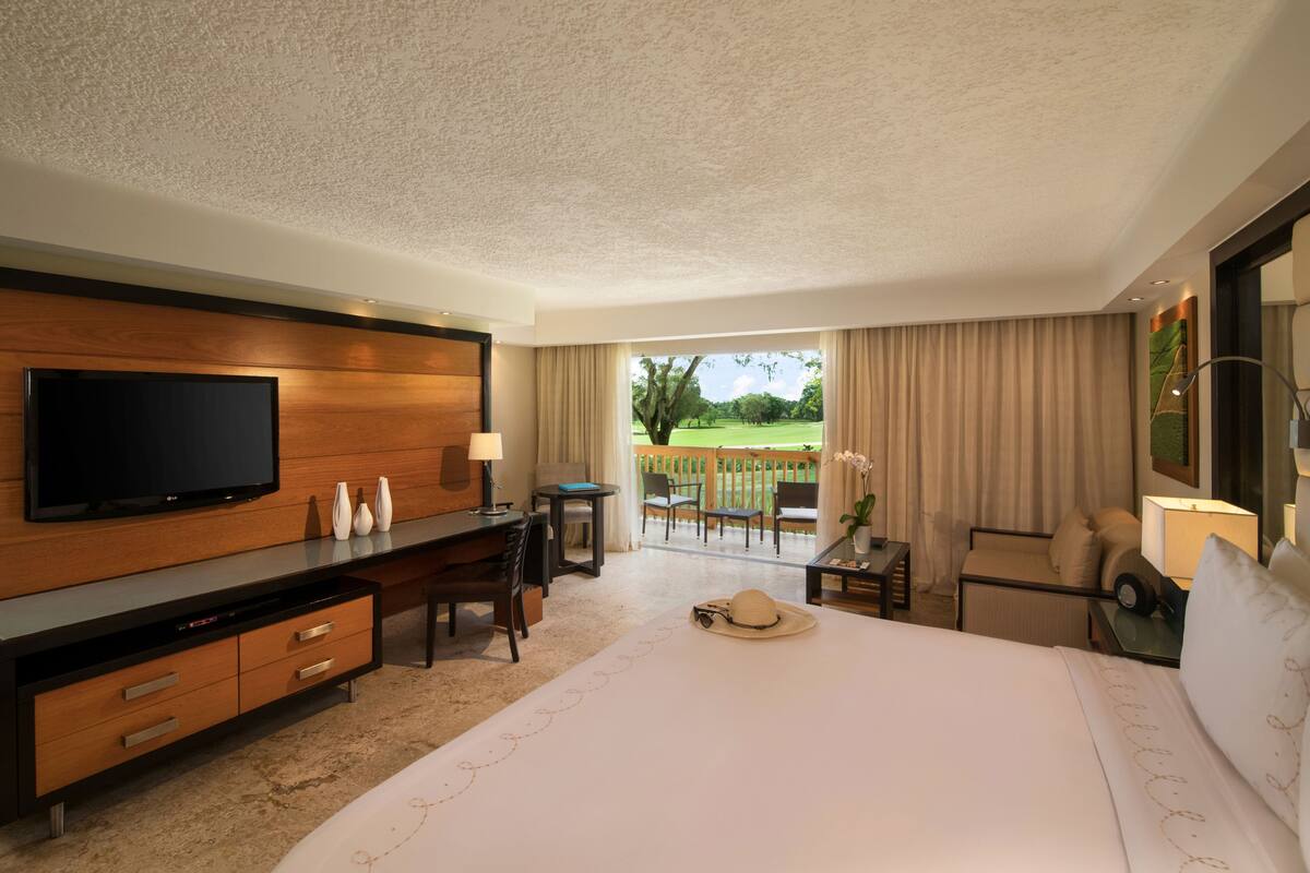 Habitación de hotel con una cama grande, televisión, escritorio y balcón con vistas al exterior.
