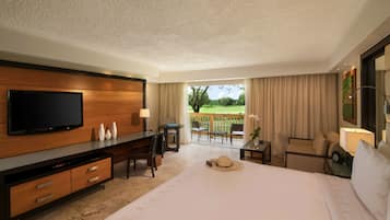 A hotel room with a large bed, a TV, a desk, and a balcony with a view of the outdoors.