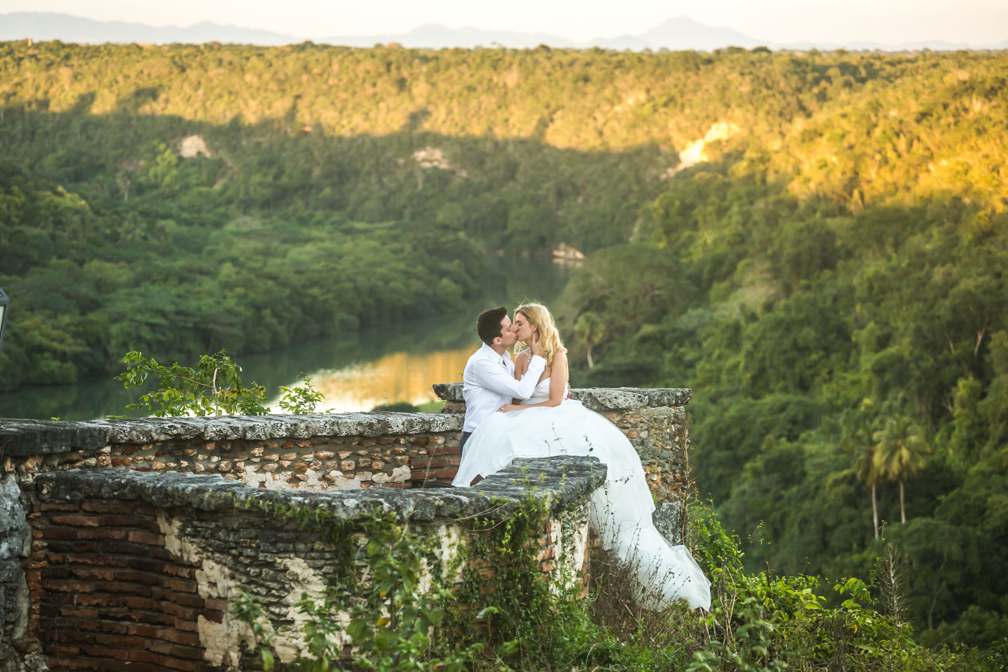 A couple embracing on a stone wall overlooking a lush green landscape.