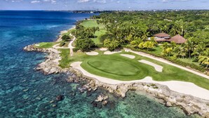 Un parcours de golf situé sur la côte, avec des eaux cristallines, une plage de sable et une végétation luxuriante.