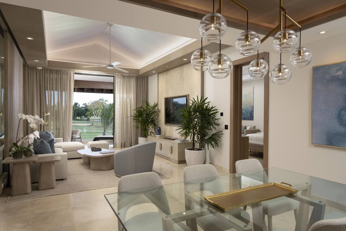 Una sala de estar moderna con una mesa de comedor de vidrio, asientos cómodos, ventanas amplias y plantas decorativas.
