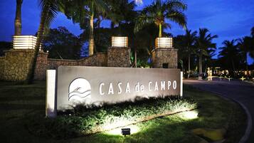 Senyal per a “CASA de CAMPO” amb un logotip, davant d'un fons de palmeres i murs de pedra, il·luminat per una llum ambiental.