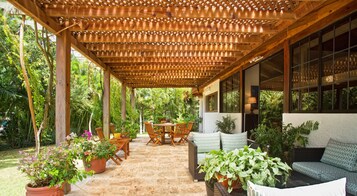 A covered patio area with a wooden pergola, outdoor seating, and potted plants.