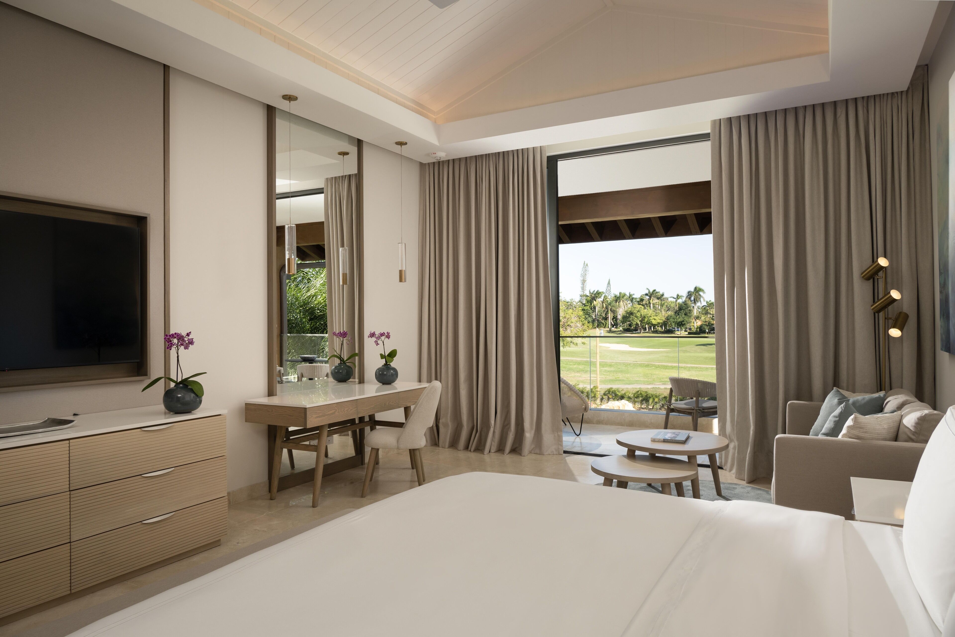 Habitación de hotel moderna con una cama grande, un escritorio, un televisor y vistas a un campo de golf.