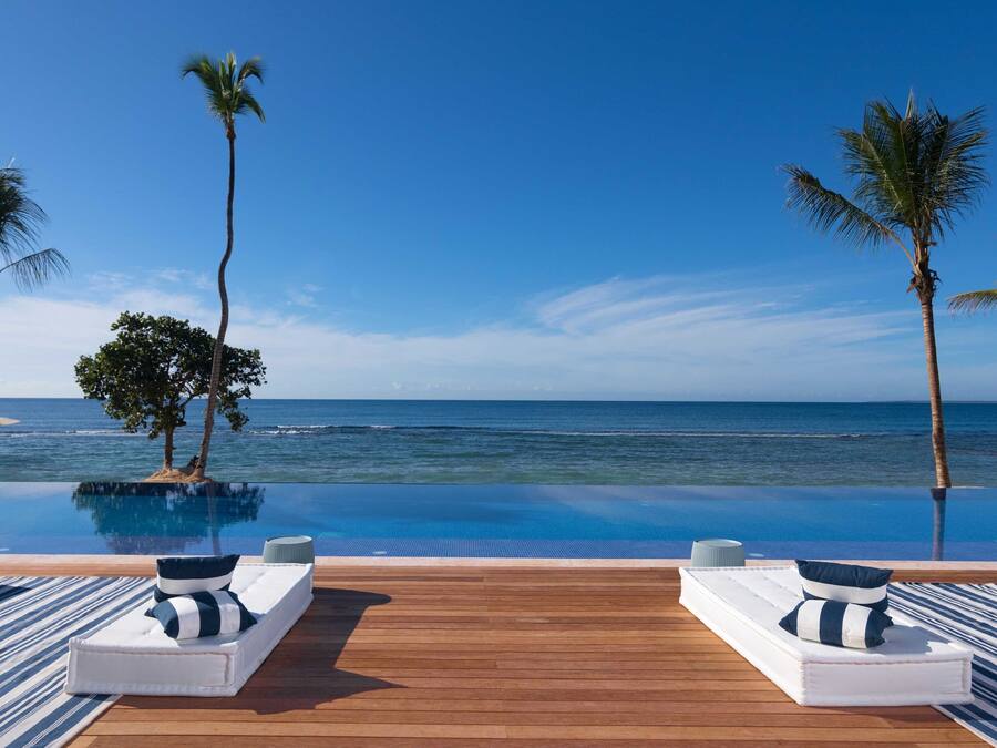 An infinity pool with wooden decking, white lounge chairs, and striped towels.