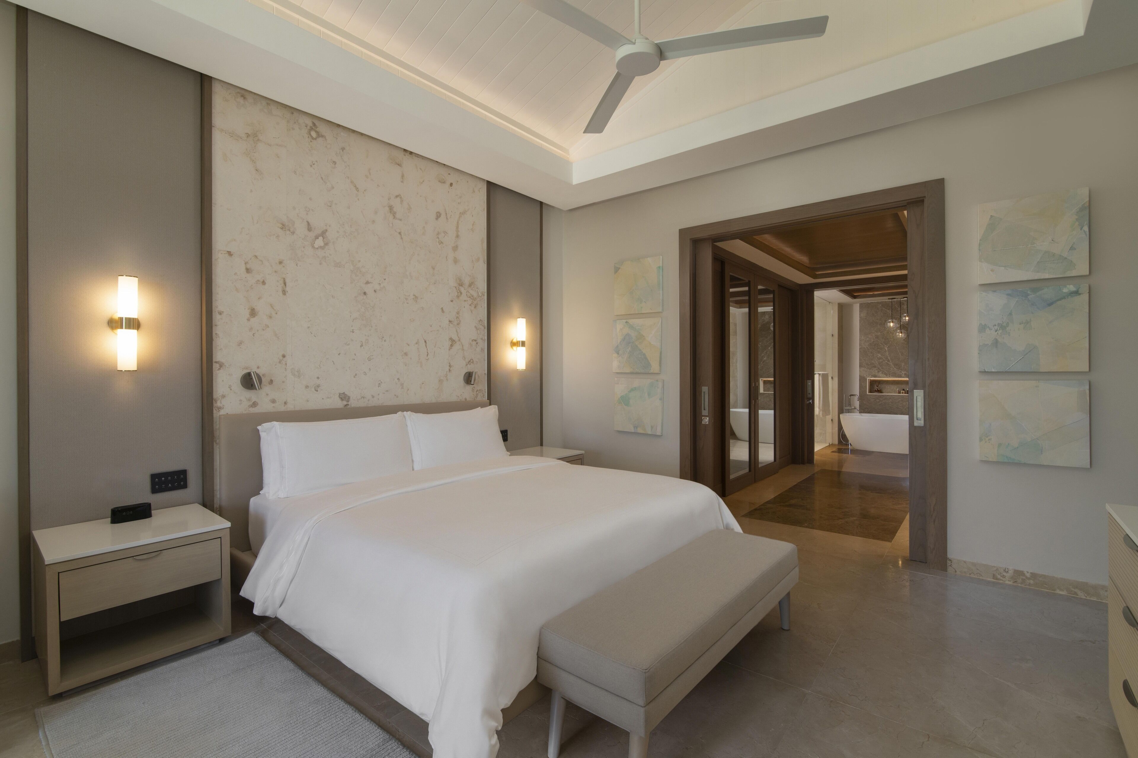 Una habitación de hotel moderna con una cama grande, mesitas de noche, un ventilador de techo y obras de arte en las paredes.