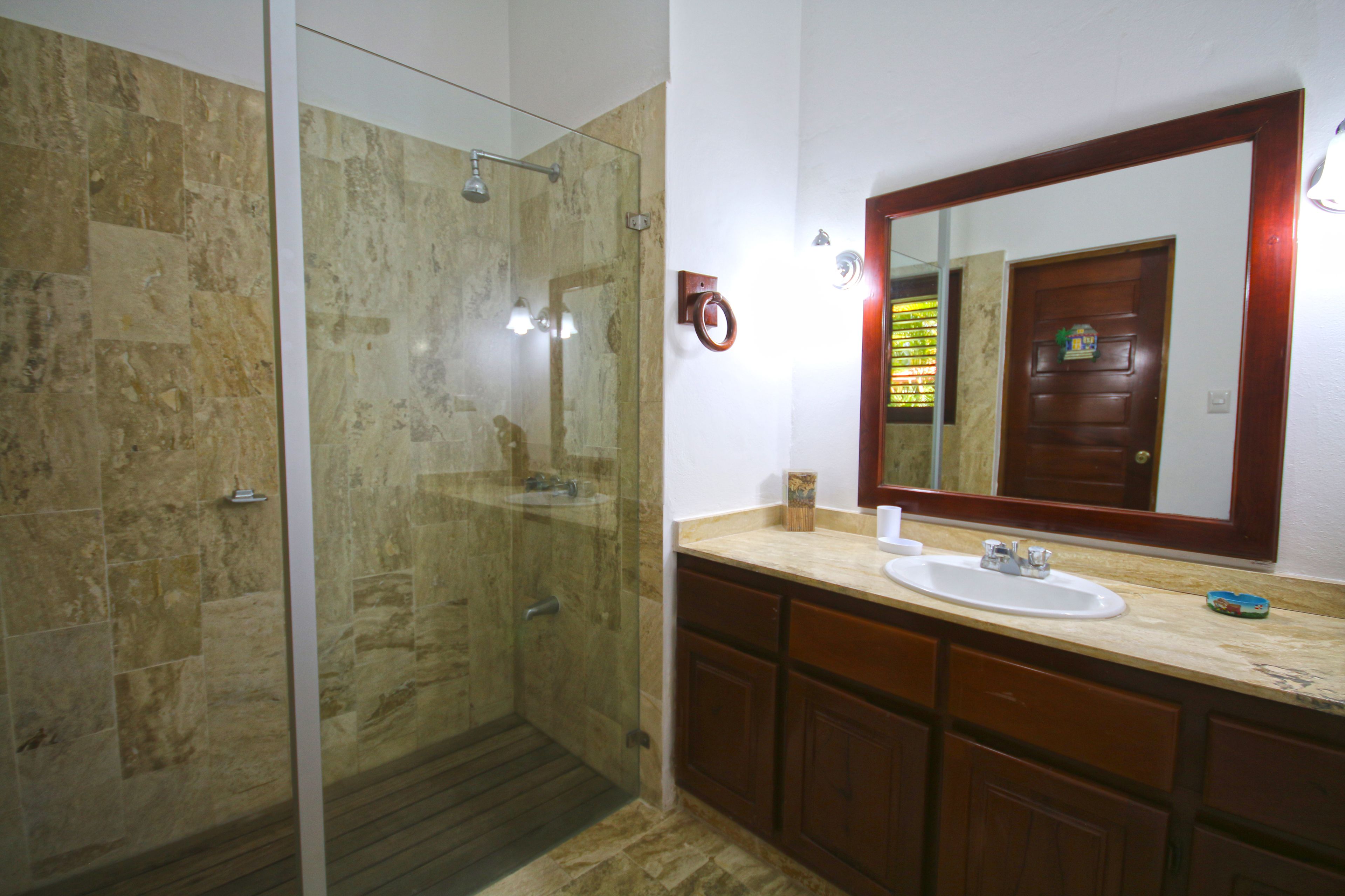 Un baño con ducha envuelta en vidrio, un lavamanos y un mueble de tocador de madera.