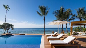 Un área junto a la piscina con sillones de descanso y vista al océano.
