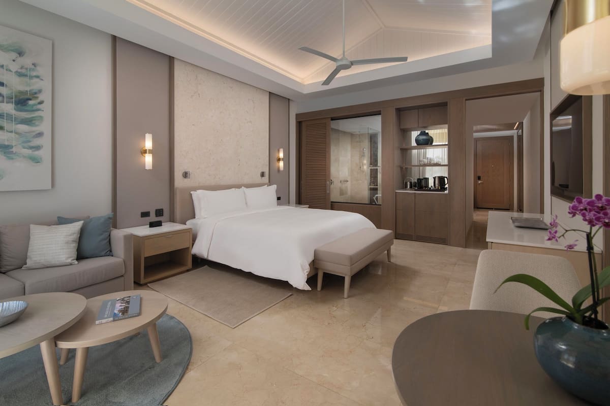 Una habitación de hotel moderna con una cama grande, un sofá, una mesita, un escritorio y un baño visible a través de una puerta abierta.