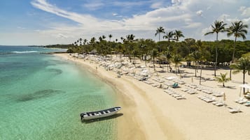 A beach with clear turquoise water, a row of sun loungers, and palm trees.
