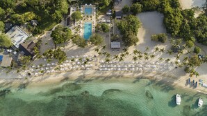 Vue aérienne d’un complexe hôtelier doté d’une piscine, d’une plage avec des transats et offrant une vue dégagée sur l’océan.