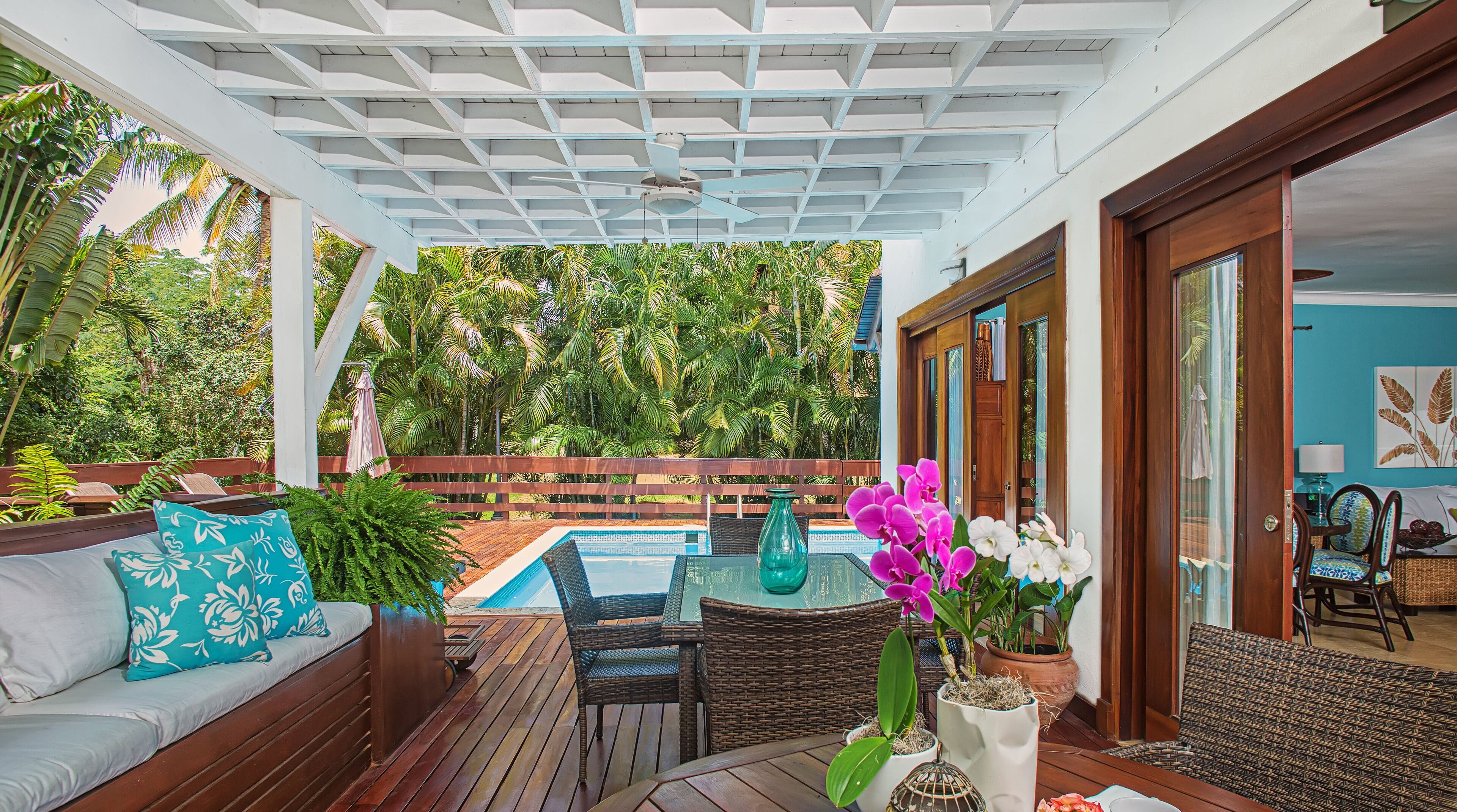 A covered outdoor area with a pool, wooden furniture, and potted plants.