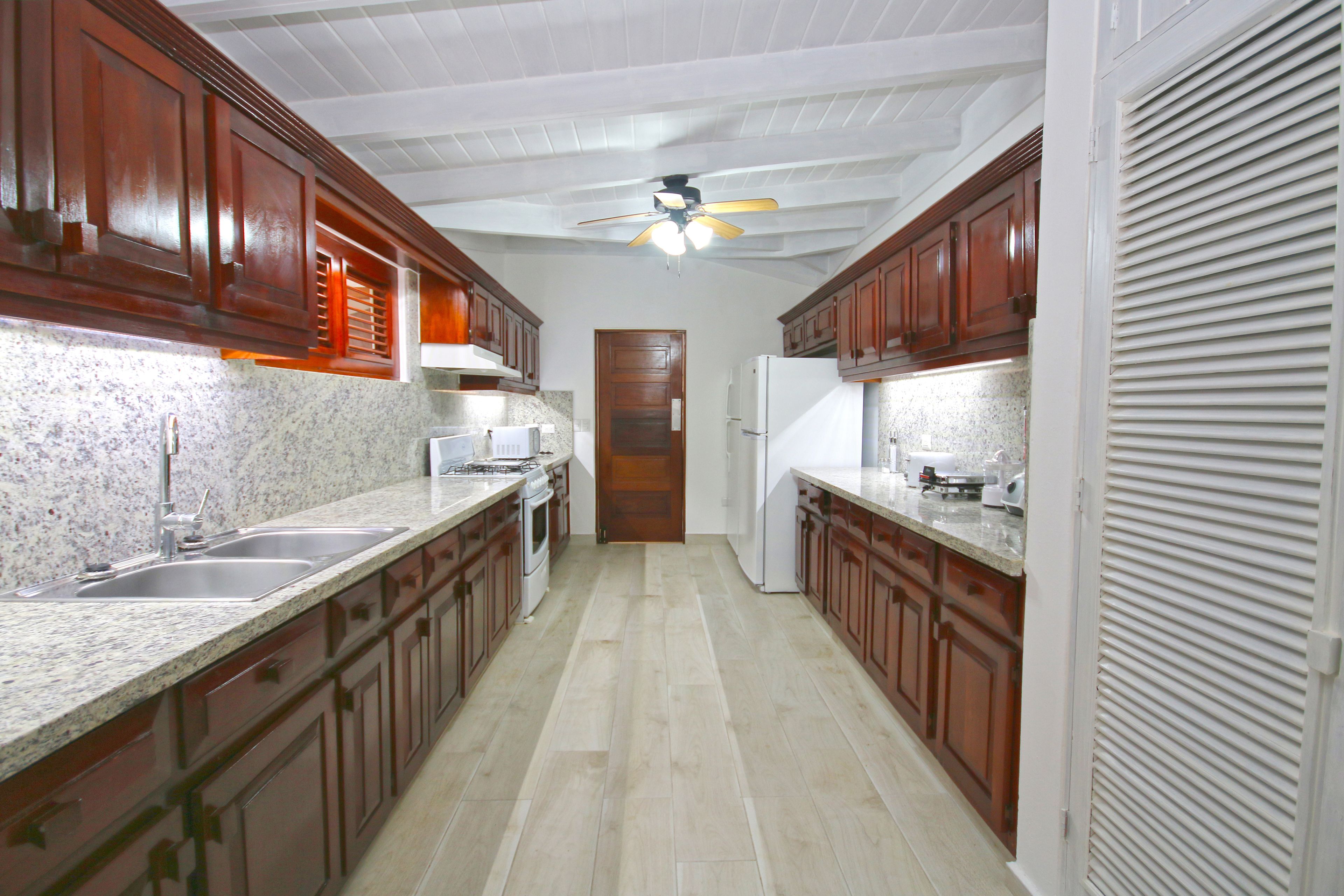 Una cocina con gabinetes de madera, encimeras de granito, horno empotrado y ventilador de techo.