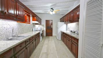 Una cocina con gabinetes de madera, encimeras de granito, horno empotrado y ventilador de techo.