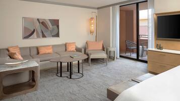 Una habitación de hotel moderna con sofá, sillón, una mesita redonda y cama. Hay un televisor y una ventana con cortinas.