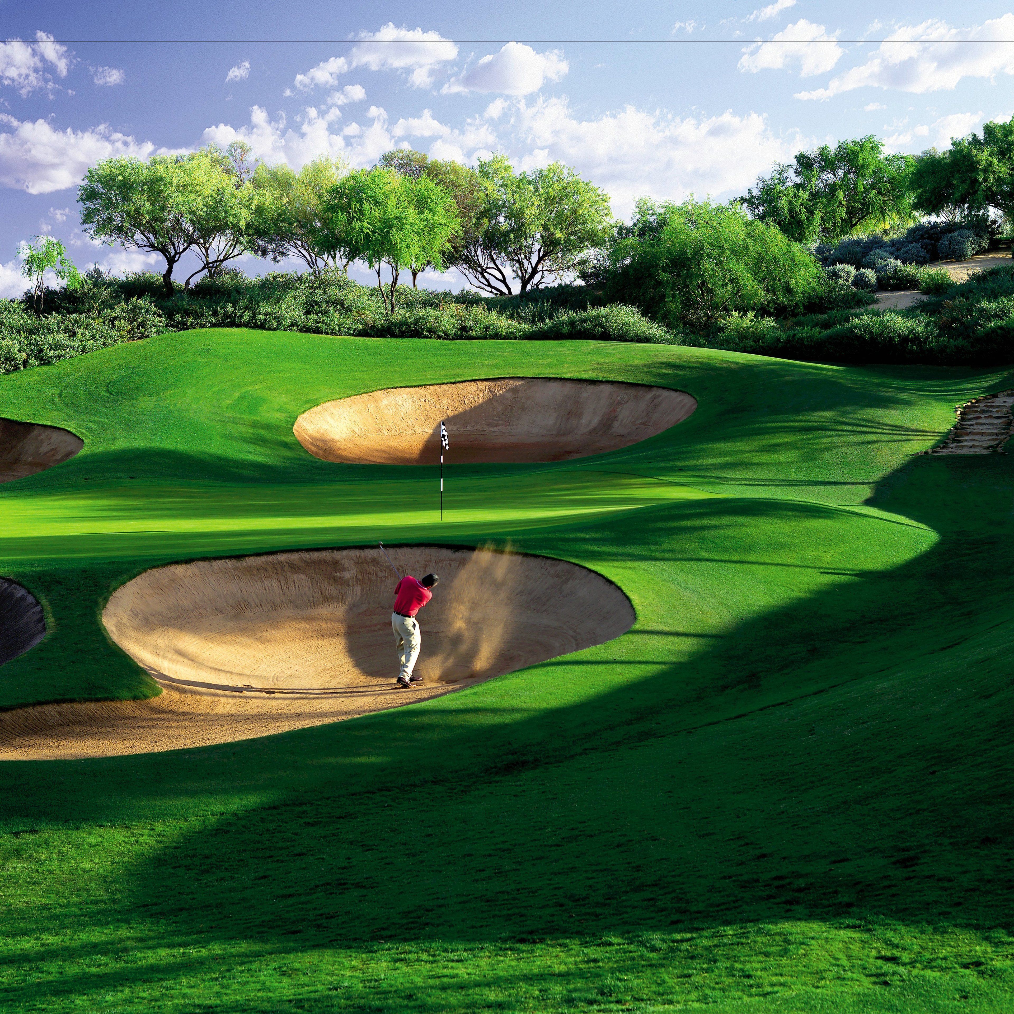 Camp de golf amb búnquers de sorra i un golfista amb samarra vermella.