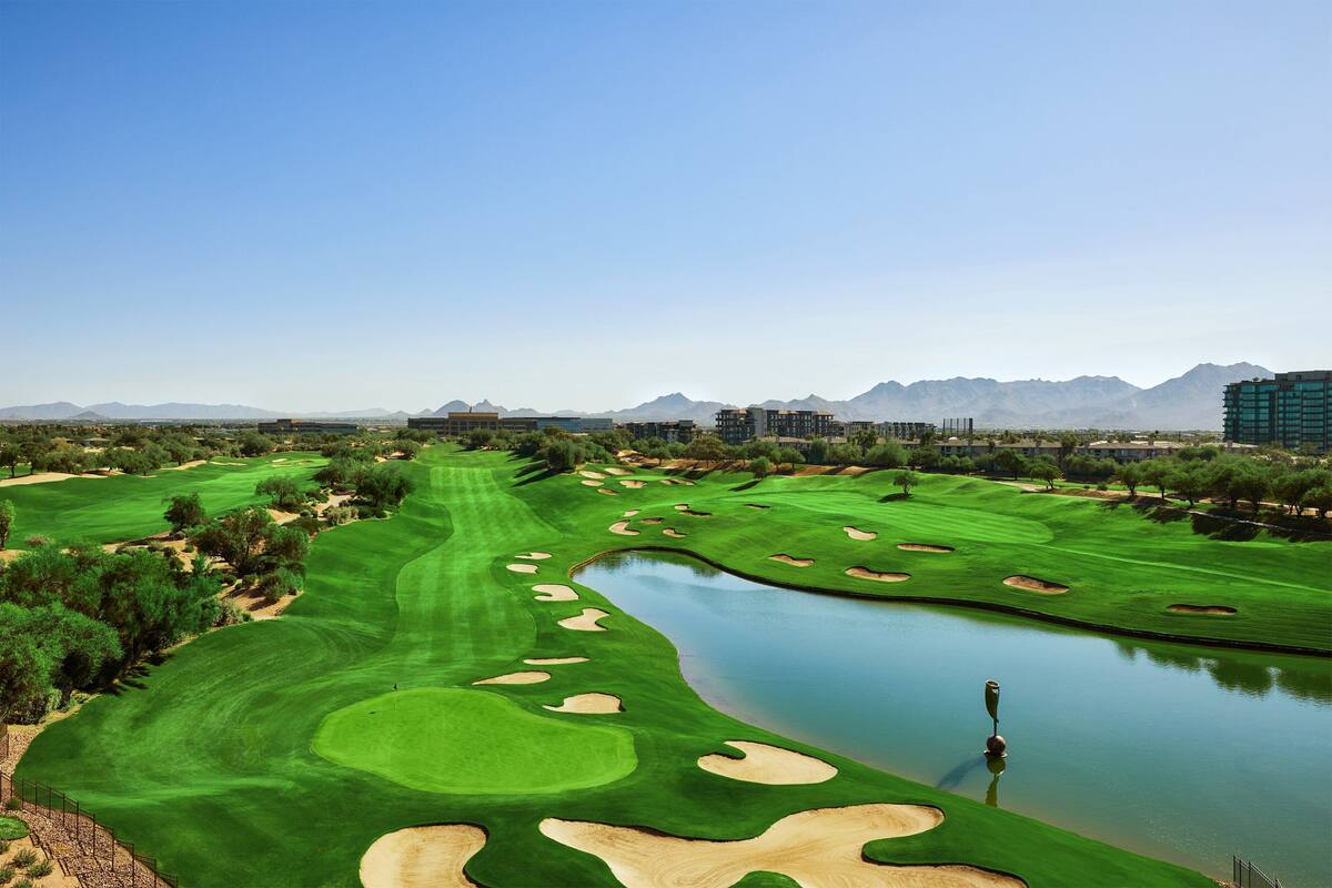 A golf course with a water hazard, sand bunkers, and distant mountains.