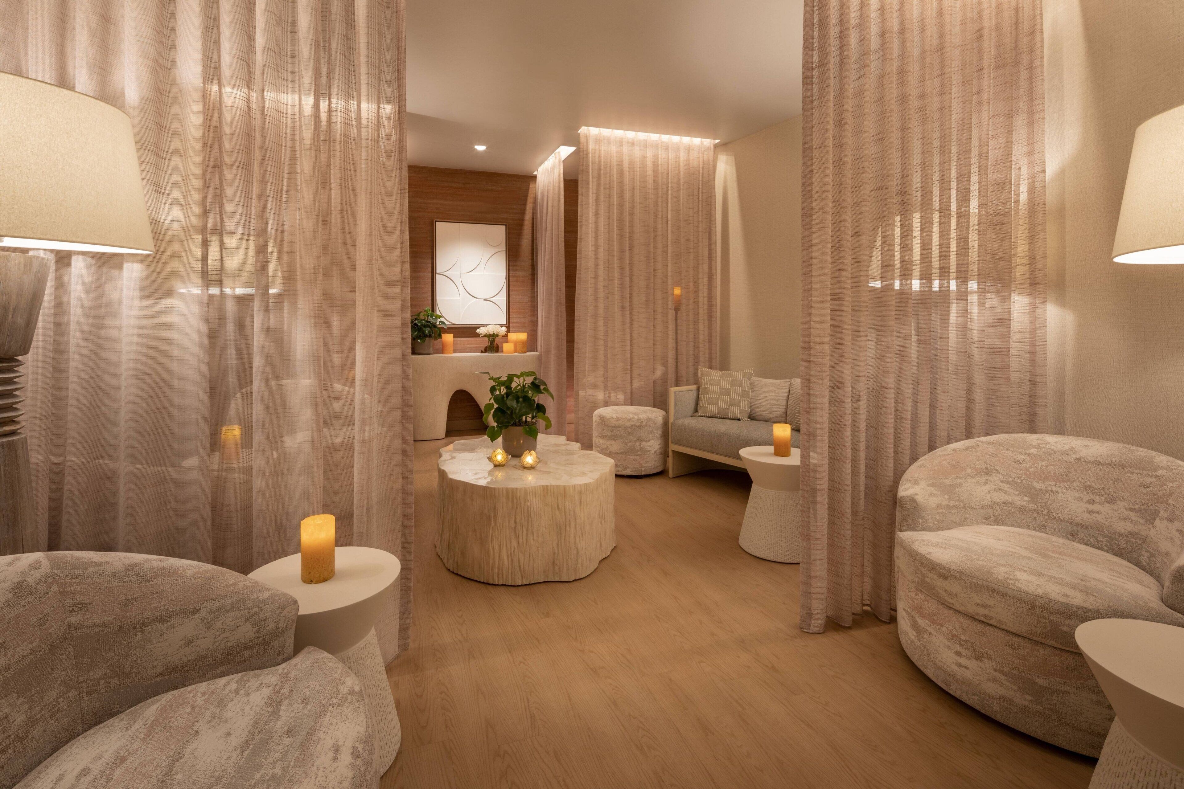 Un spa moderno con una mesa redonda de madera, dos zonas de descanso acolchadas y una pequeña planta decorativa.