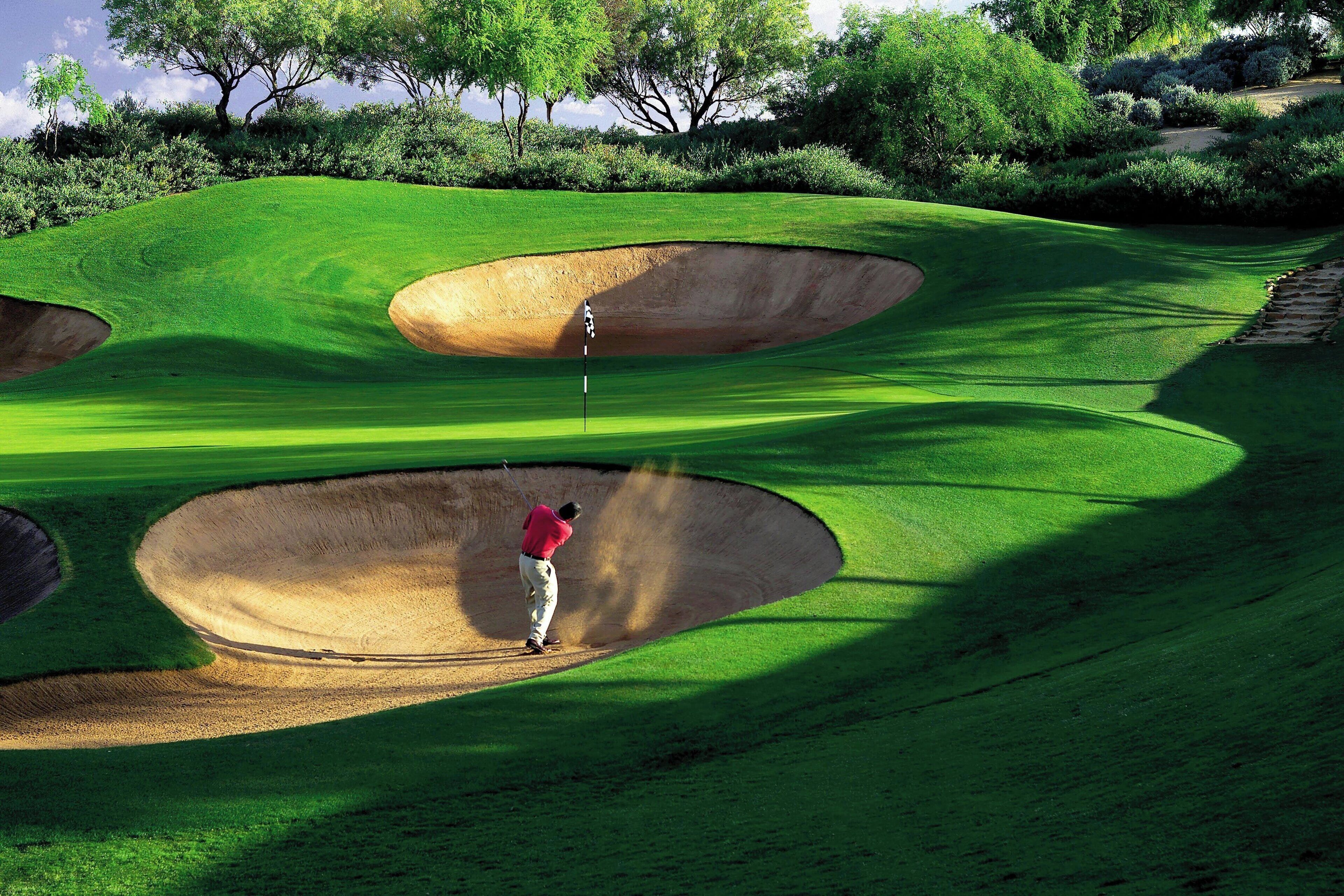 Un campo de golf con búnkeres y un golfista con camisa roja.