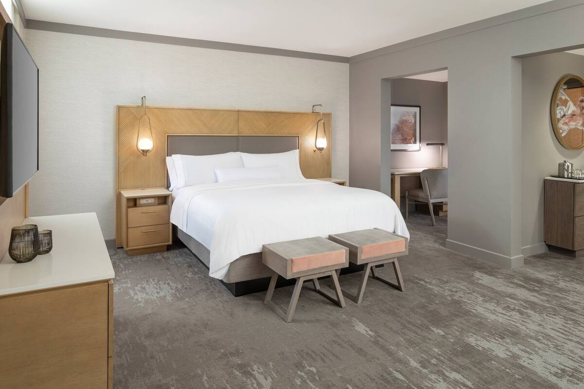 A modern hotel room with a large bed, bedside tables, a desk, and a seating area.
