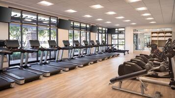 Un gimnasio con múltiples cintas de correr alineadas, amplias ventanas y diverso equipamiento de ejercicio.