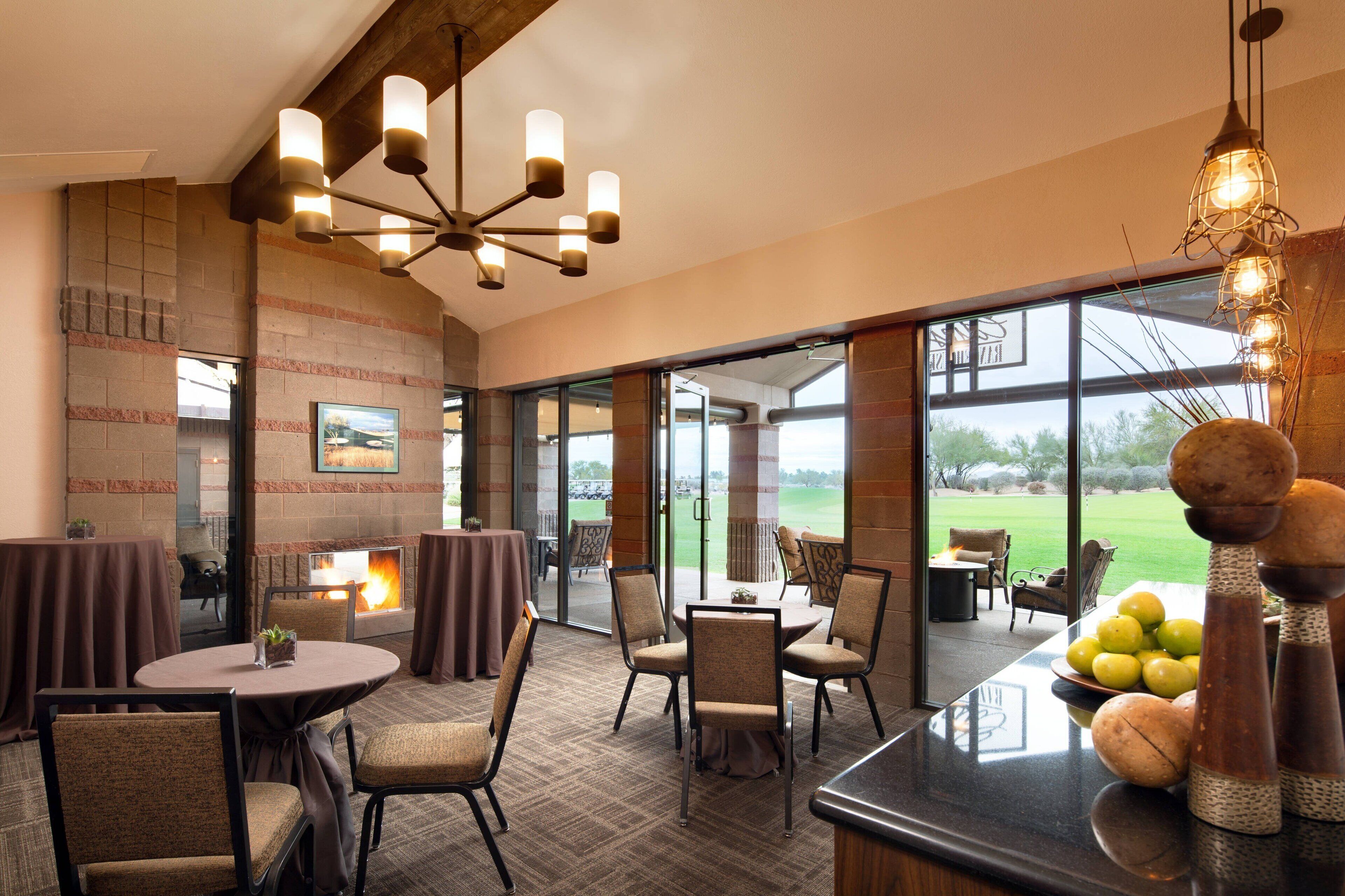 A restaurant with a fireplace, round tables, and chairs. There is a view of a golf course through large windows.