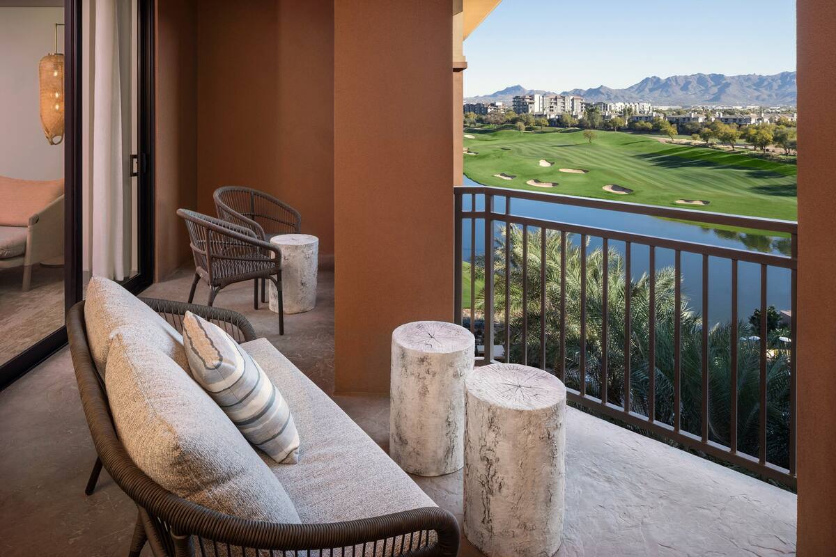 A balcony with a view of a golf course, a sofa, two chairs, and two round tables.