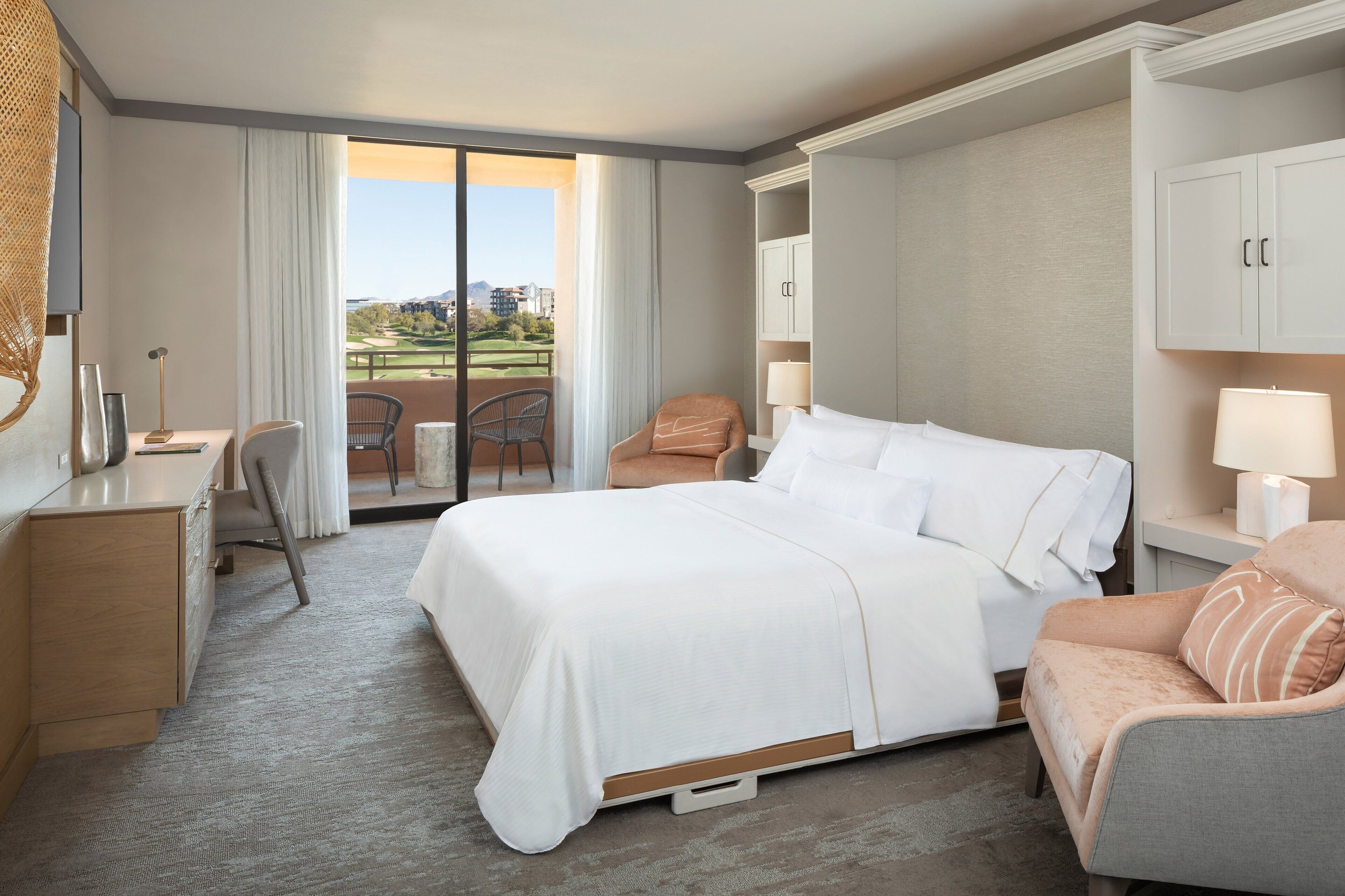 Habitación de hotel con una cama grande, un escritorio, una silla y vista a un campo de golf.