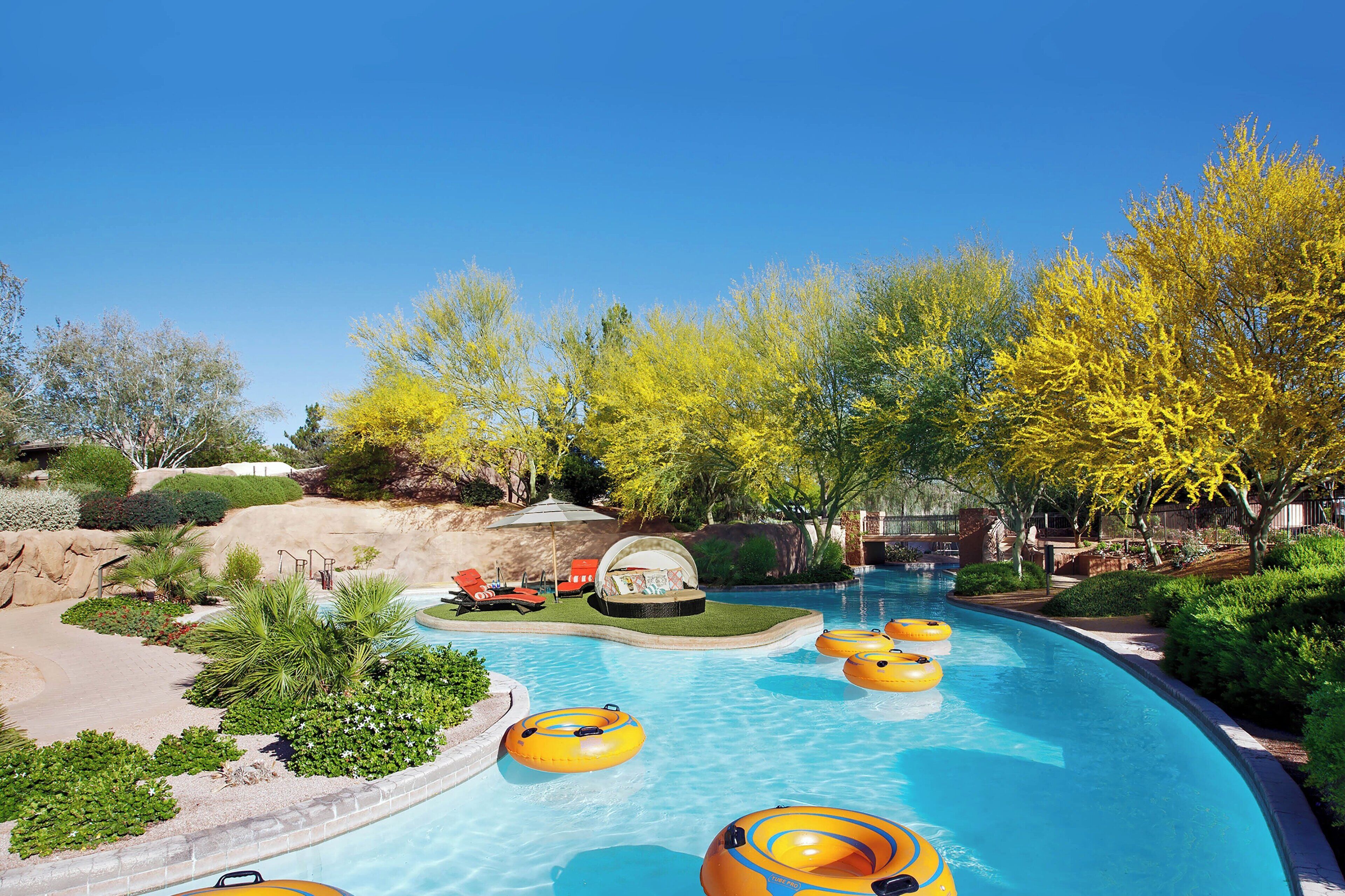Una piscina con flotadores, rodeada de zonas ajardinadas y árboles.