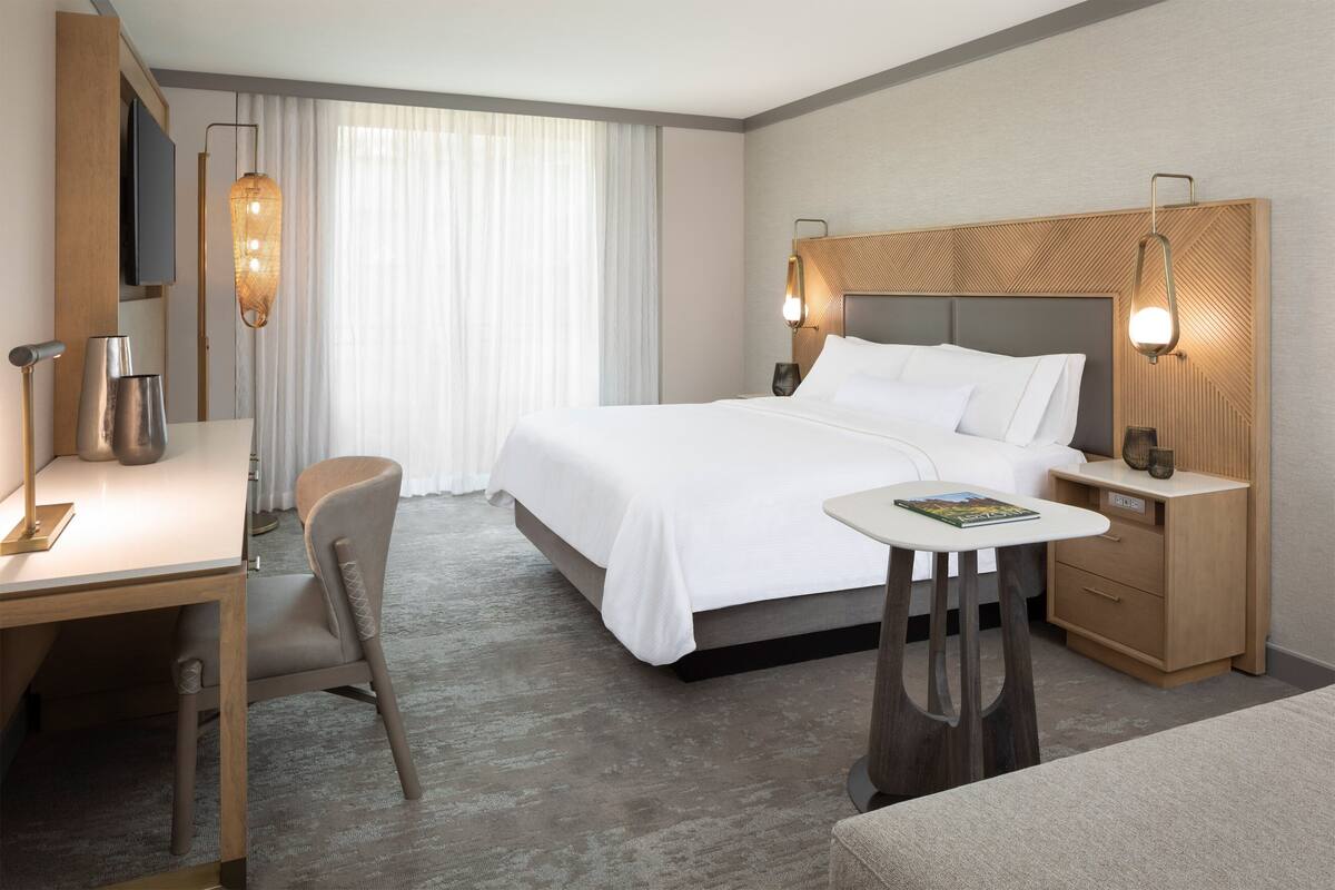 A hotel room with a bed, bedside tables, a desk, a chair, and a TV mounted on the wall.