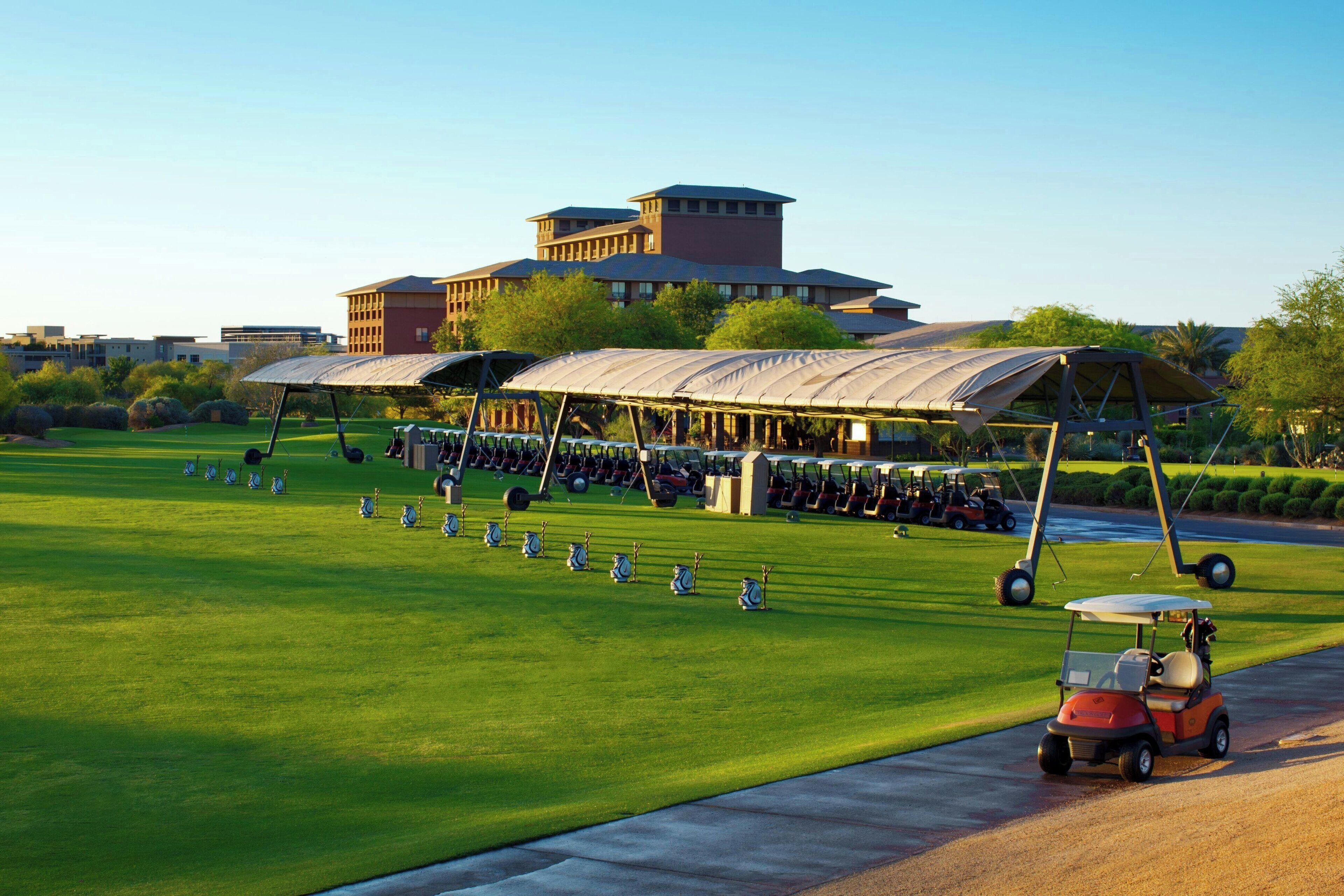 Un campo de golf con un club de campo, un campo de prácticas techado y un carrito de golf en la carretera.
