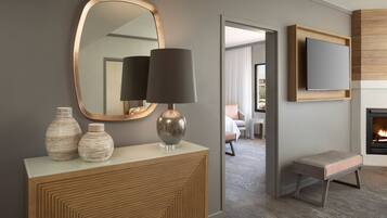 Un salon moderne avec un grand miroir, une console ornée de vases décoratifs, une lampe sur pied, un téléviseur fixé au mur et un petit banc.
